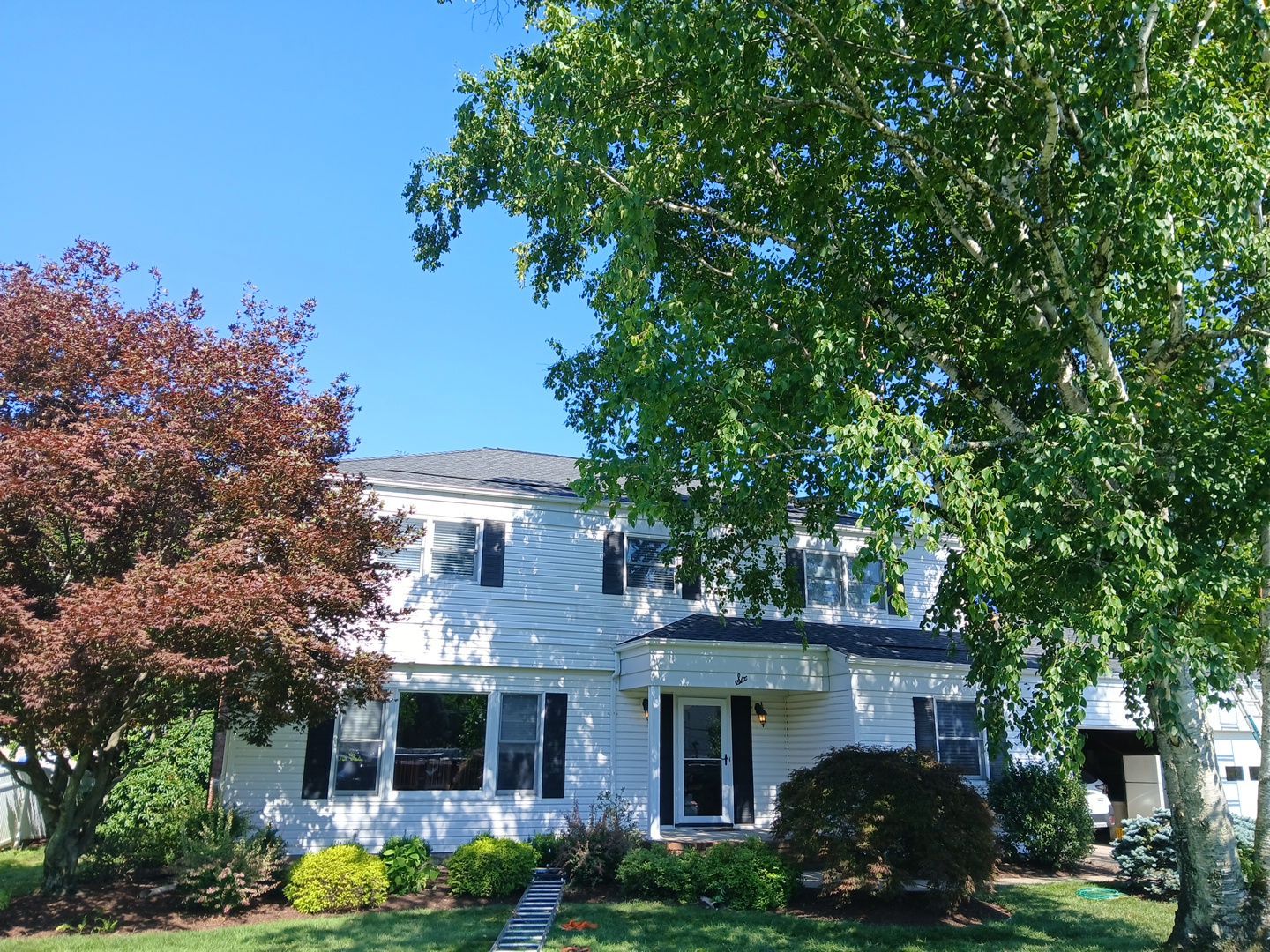 Street view of a completed white colonial with new dark shingle roof and mature trees in North Jersey