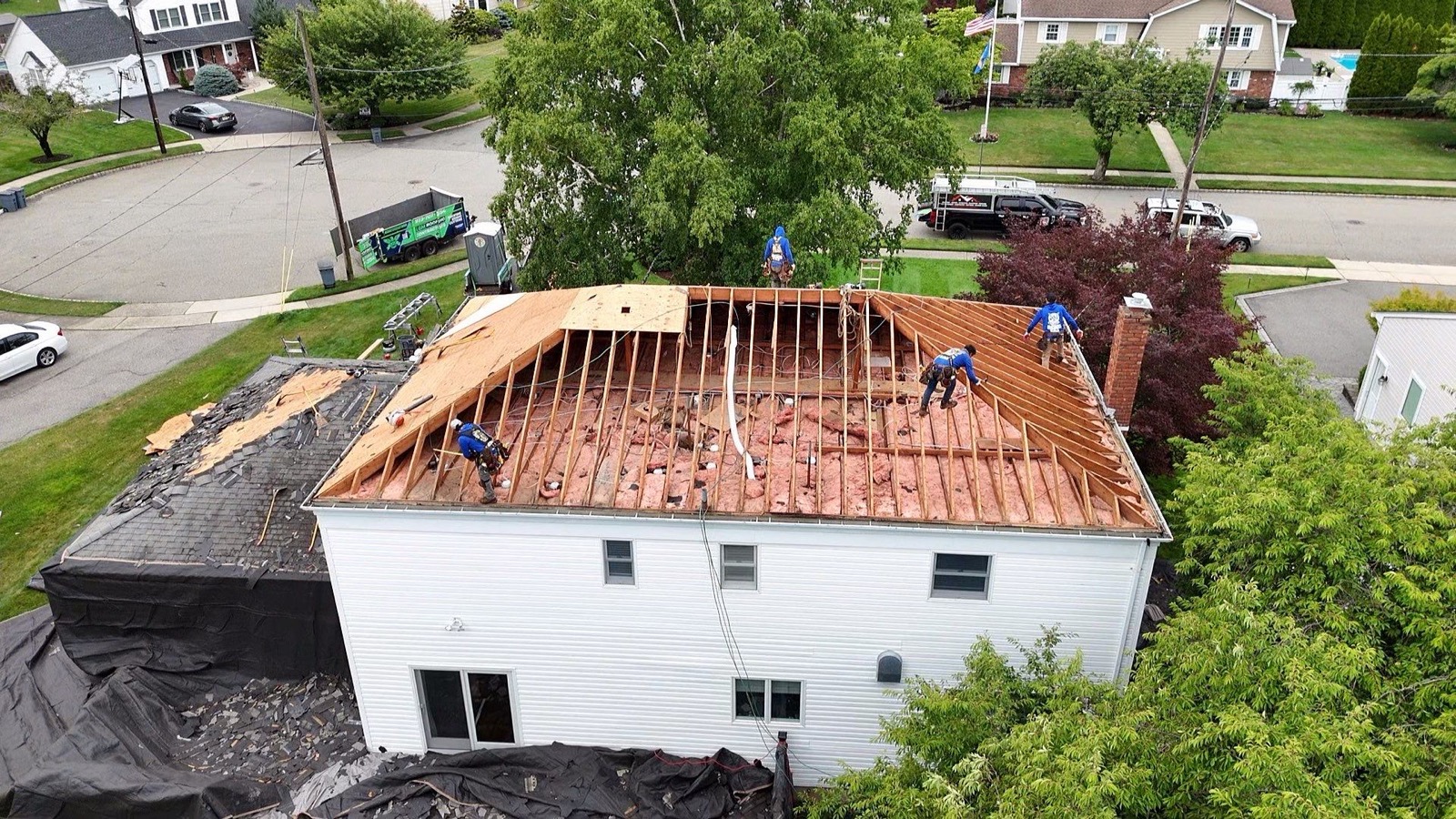 Drone view of LGM crew resheathing a ranch with exposed rafters and pink insulation visible