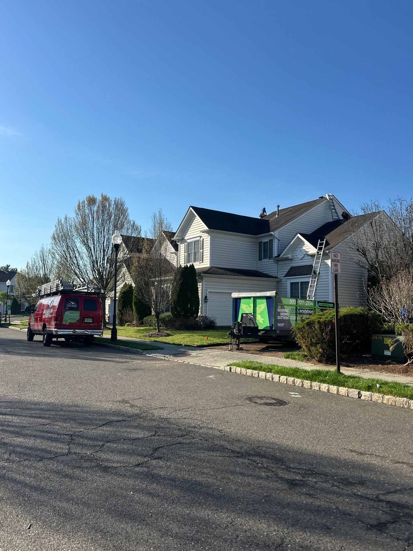 Street view of LGM trucks and dumpster trailer arriving at a suburban colonial for a full roof replacement