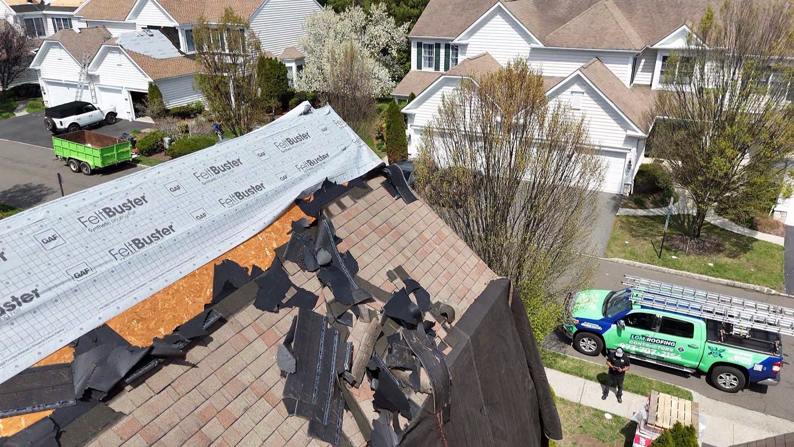 LGM crew on a suburban roof with FeltBuster underlayment, green LGM trucks parked below