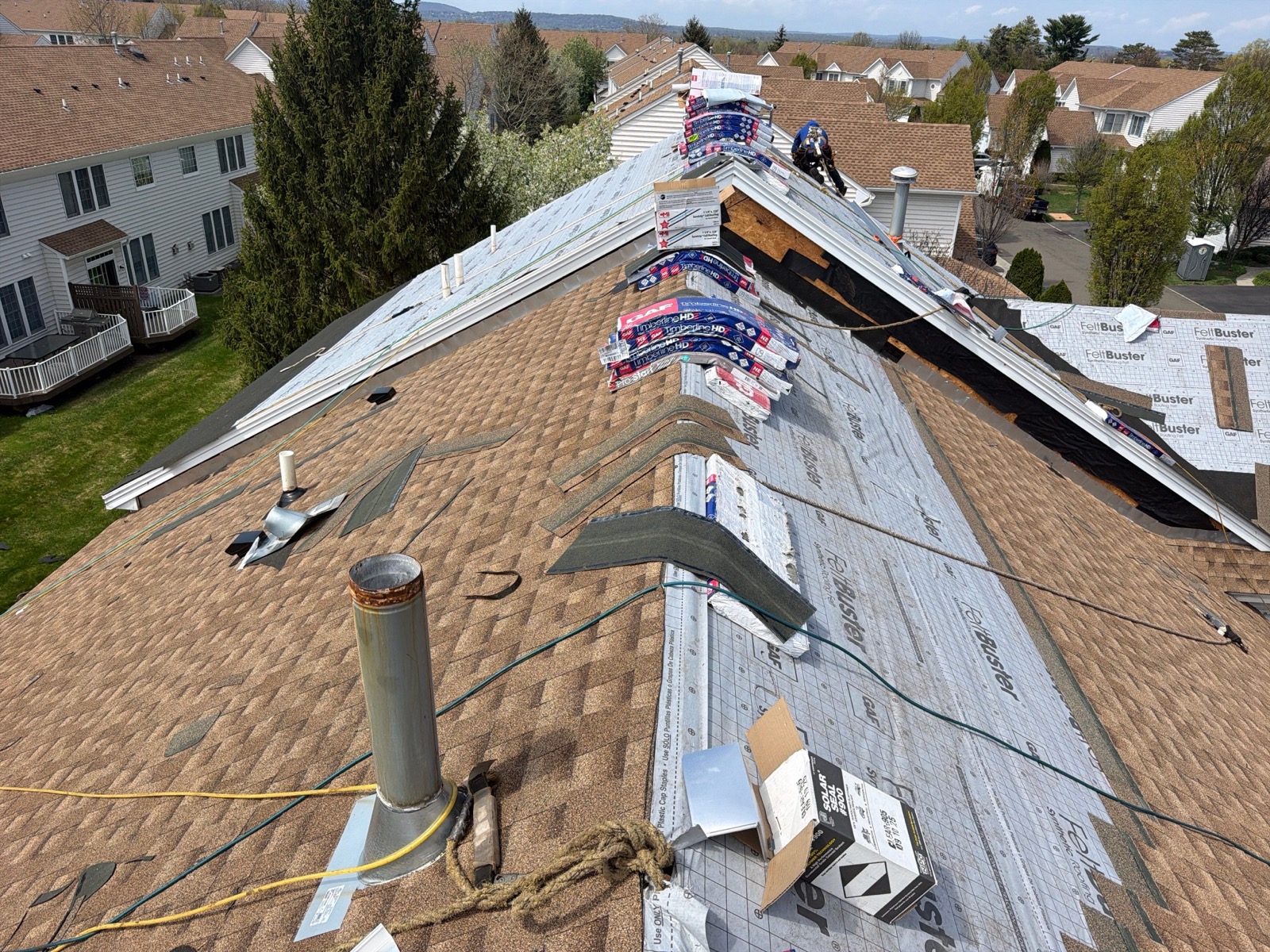 Close-up of GAF Timberline HDZ shingle bundles staged at a suburban roof ridge with FeltBuster below