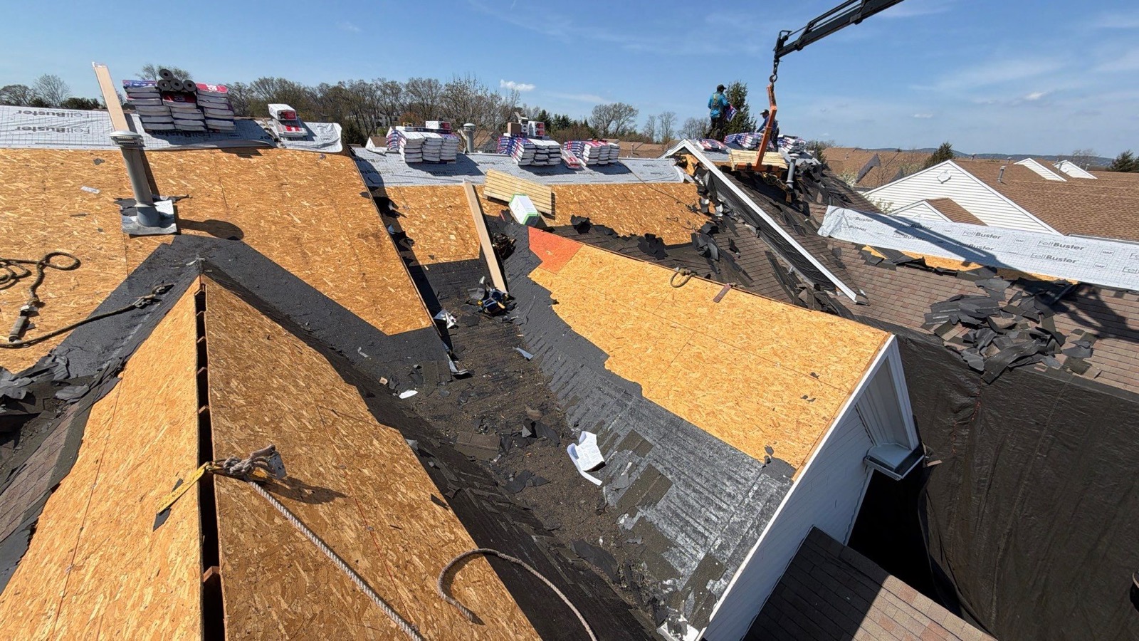 Aerial view of GAF Timberline HDZ bundles and FeltBuster rolls staged along a suburban roof ridge