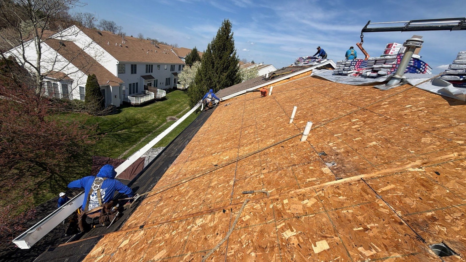LGM crew resheathing a large suburban roof with new plywood and GAF Timberline bundles staged at the ridge