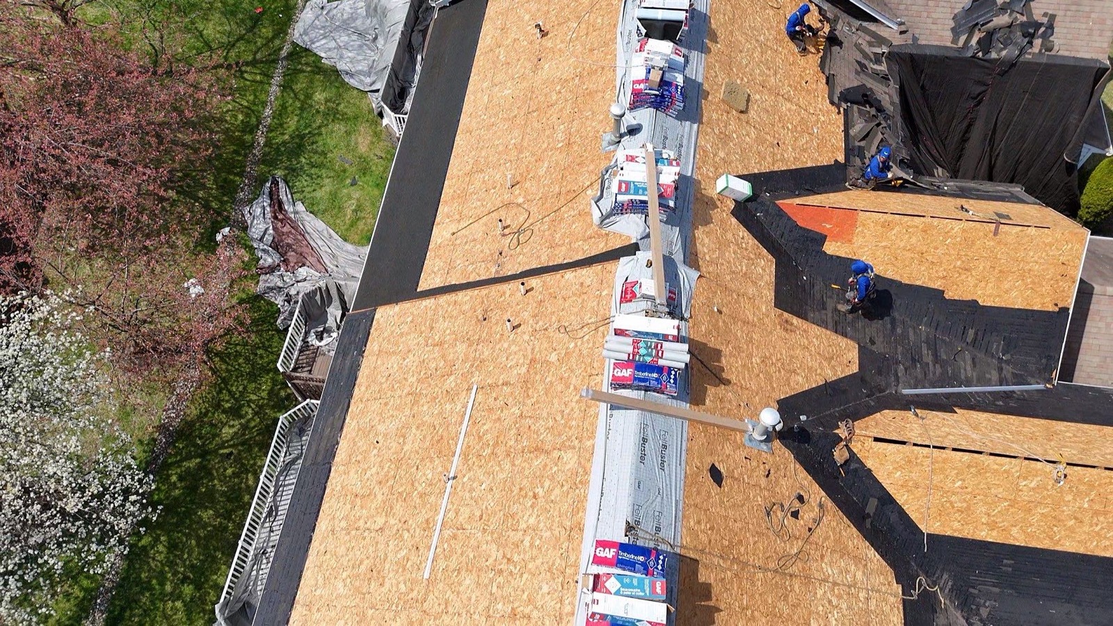 Overhead drone shot of a suburban roof with GAF bundles and FeltBuster rolls lined up along the ridgeline