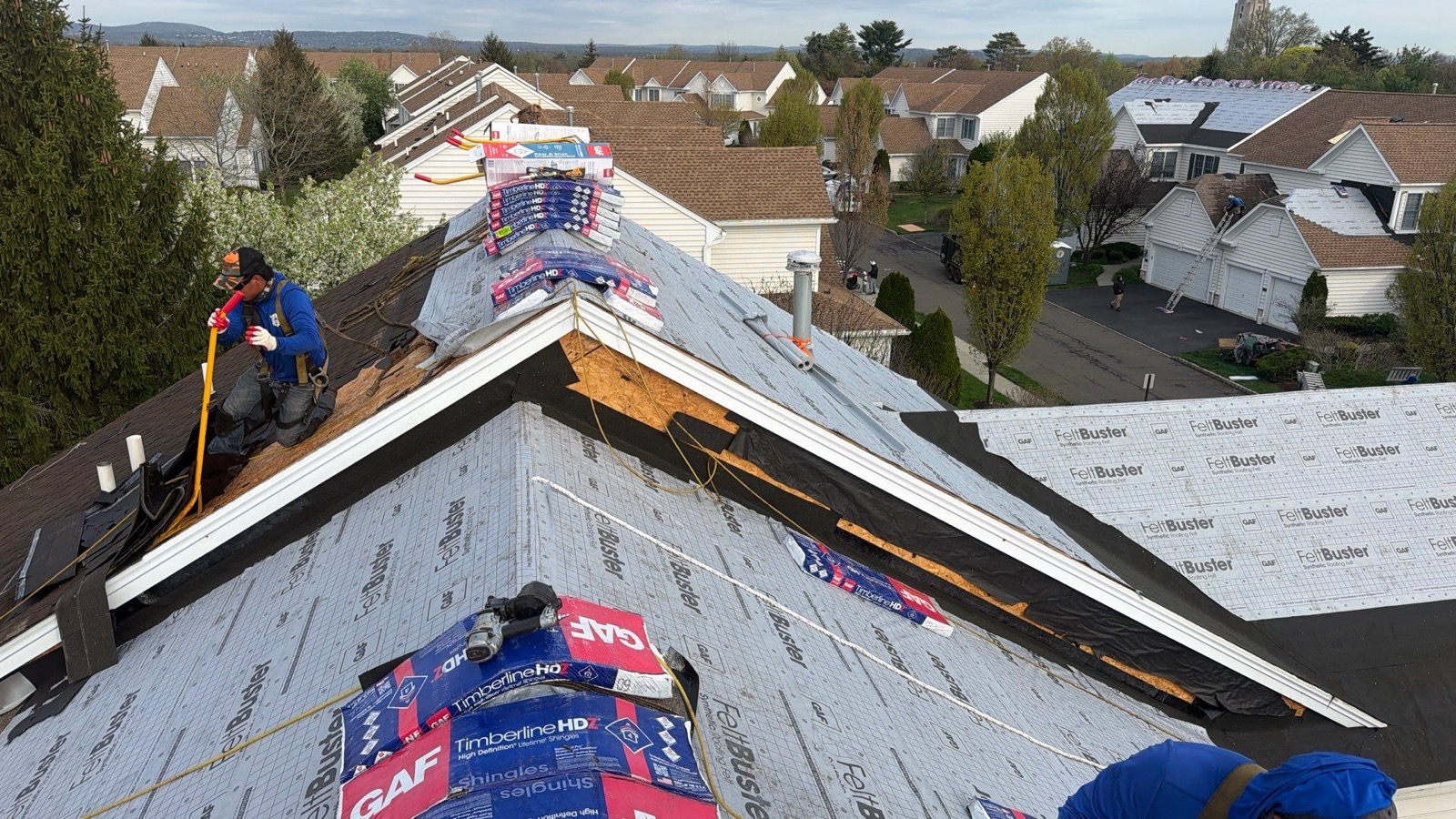 LGM crew member at the ridge of a suburban roof with GAF Timberline HDZ shingle bundles stacked and ready
