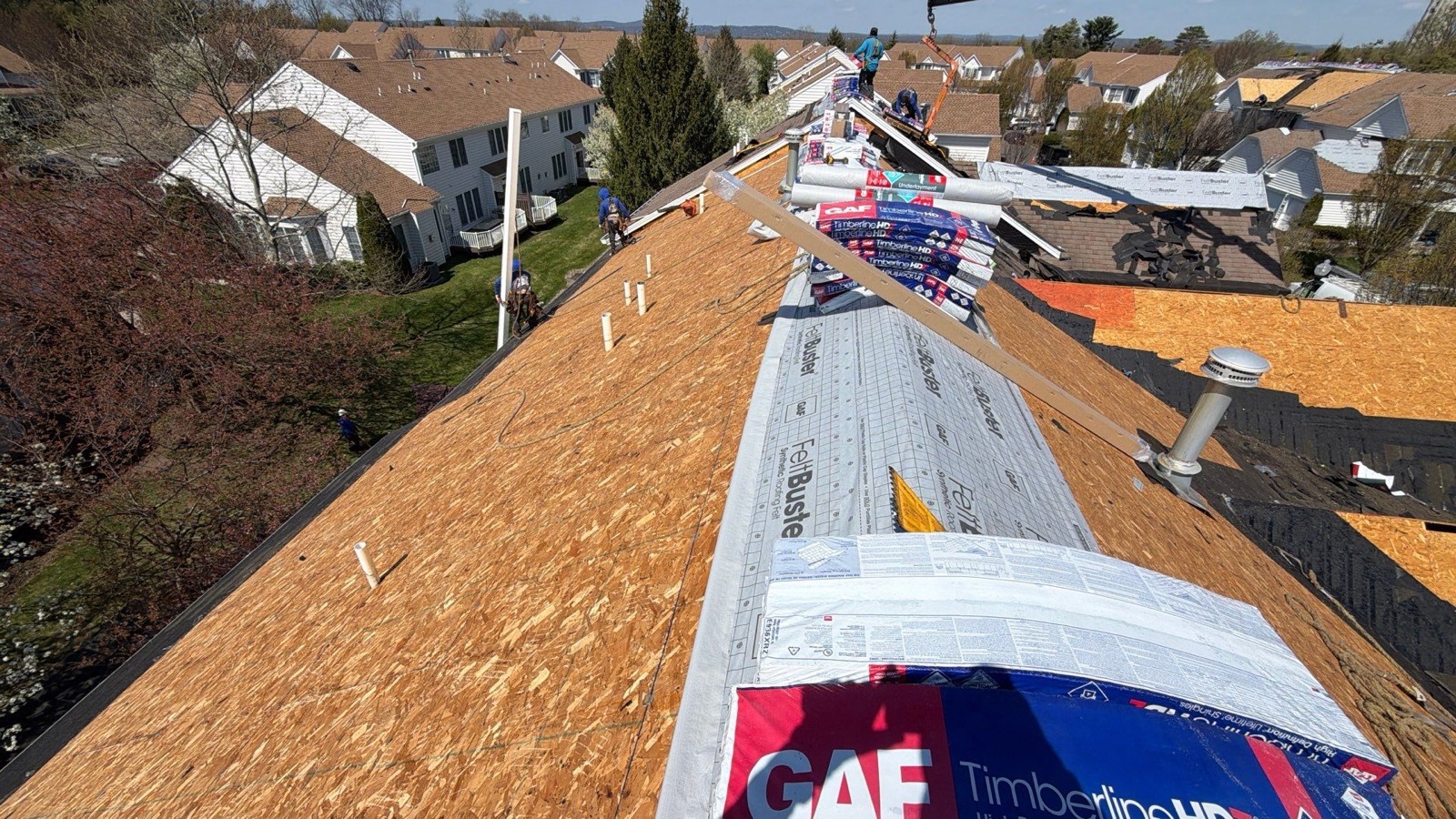 LGM crew in blue stripping old shingles on a steep suburban roof with OSB decking exposed