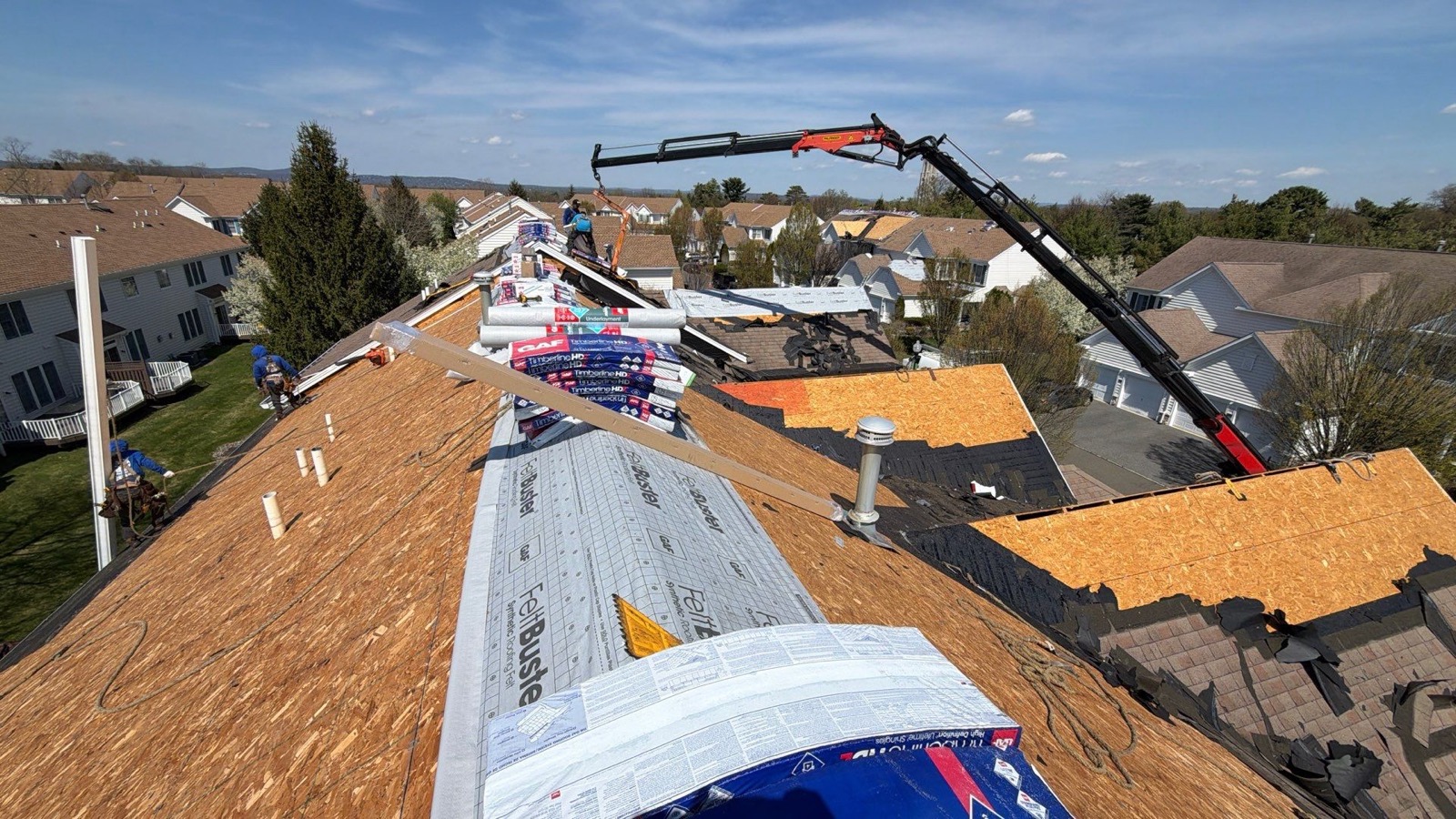 Drone view of LGM crew mid-tear-off on a suburban colonial with exposed decking and old shingles