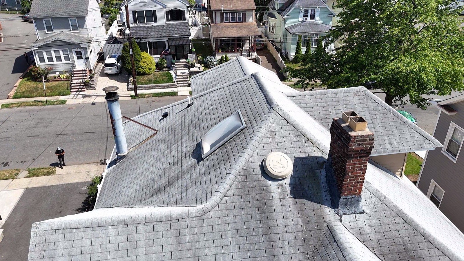 Side angle of a completed Victorian roof replacement with new tan GAF shingles and clean ridge caps