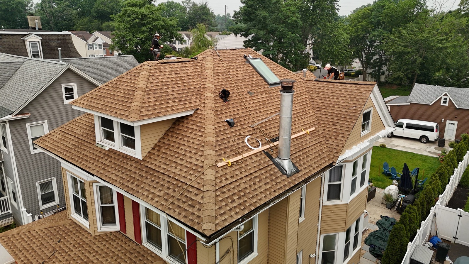 Drone view of a Victorian roof nearly completed with new tan GAF shingles and crew finishing the last section