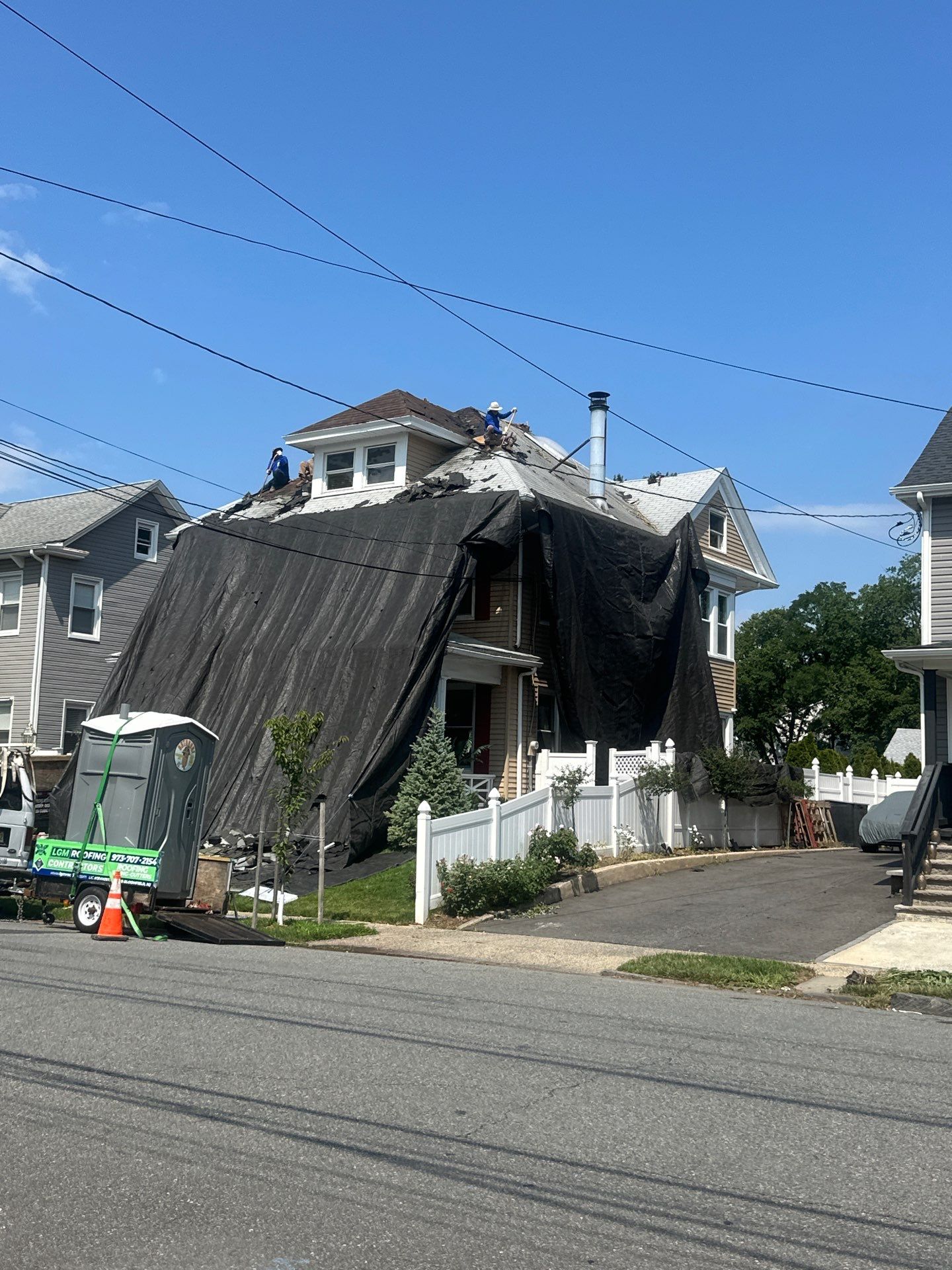 Street view of LGM crew tearing off an old roof on a Victorian home with protective tarps draped over the facade