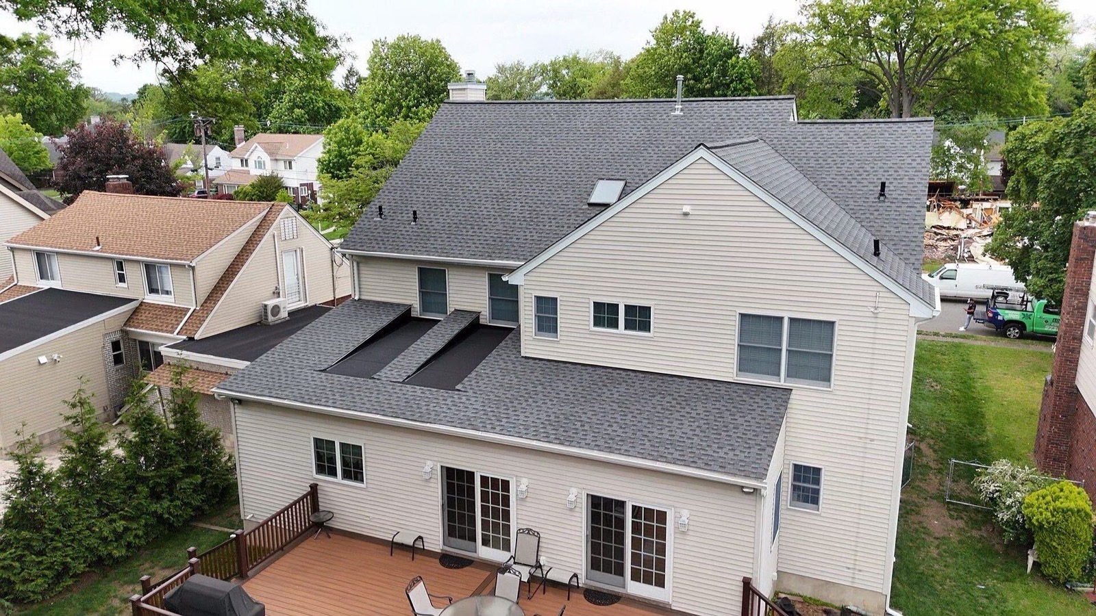 Drone view of a completed roof replacement showing new shingles and flat-roof transition on a two-story home