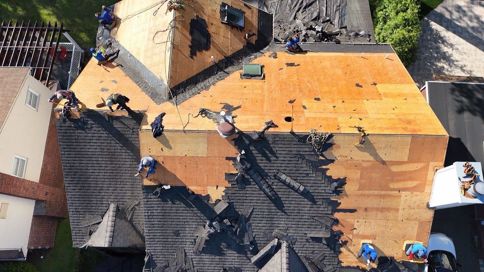 Aerial view of LGM crew stripping shingles to expose plywood decking on a large residential roof