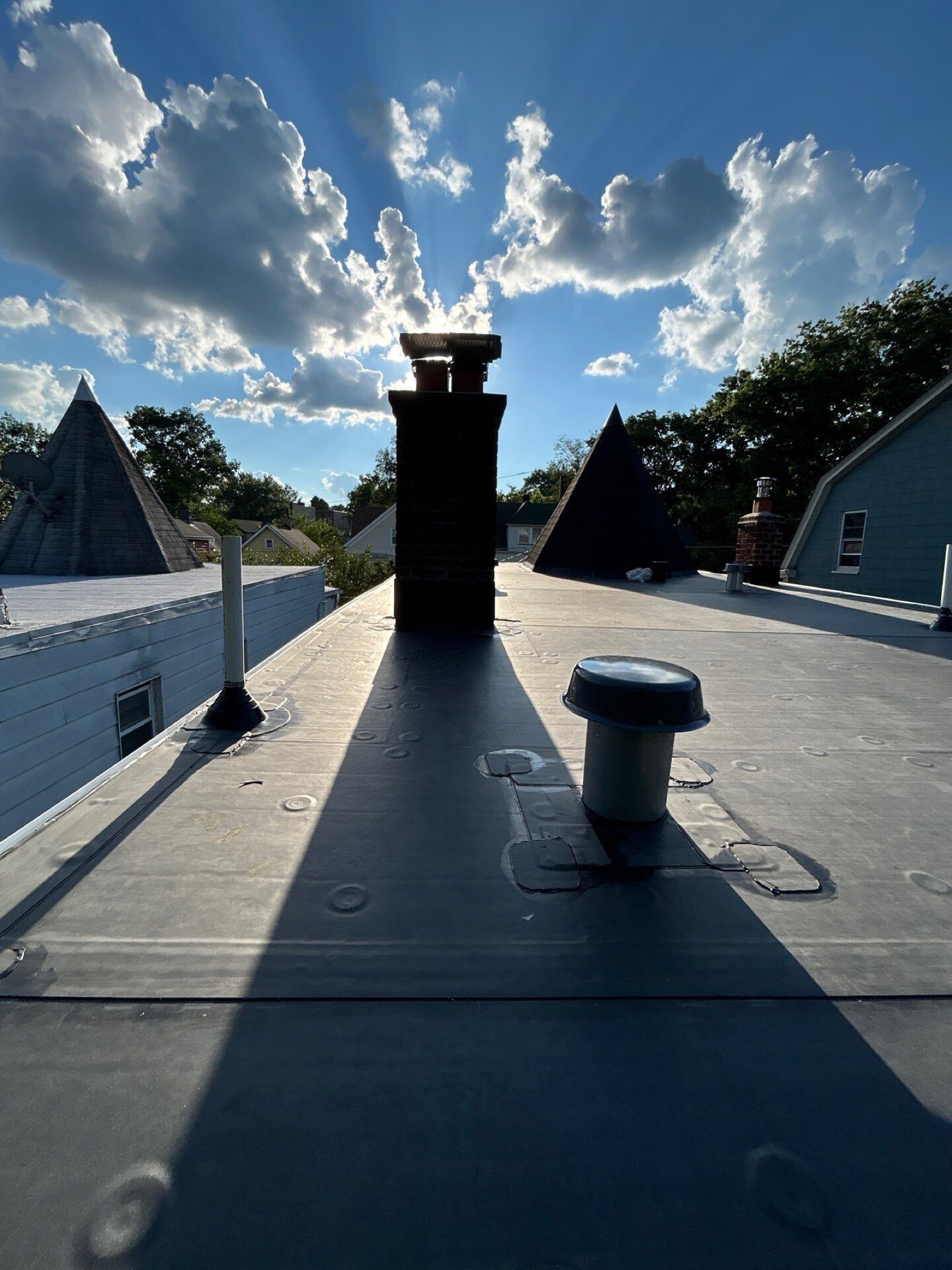 Completed EPDM flat roof with chimney and pipe boots silhouetted at sunset over North Jersey