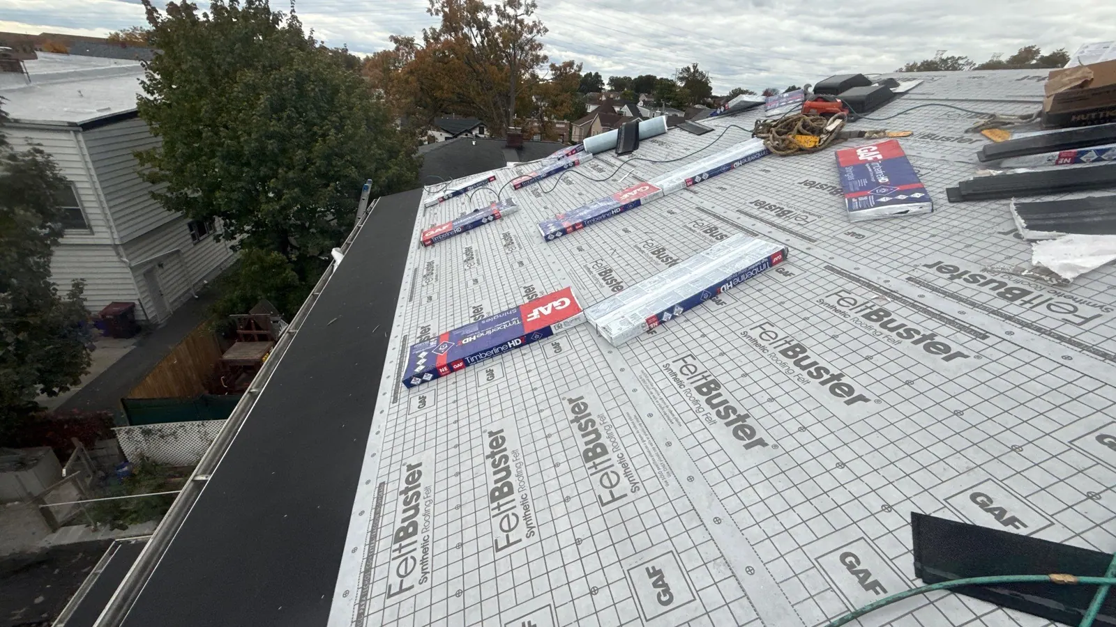 Synthetic underlayment rolled out across a roof deck with GAF shingle bundles staged on top